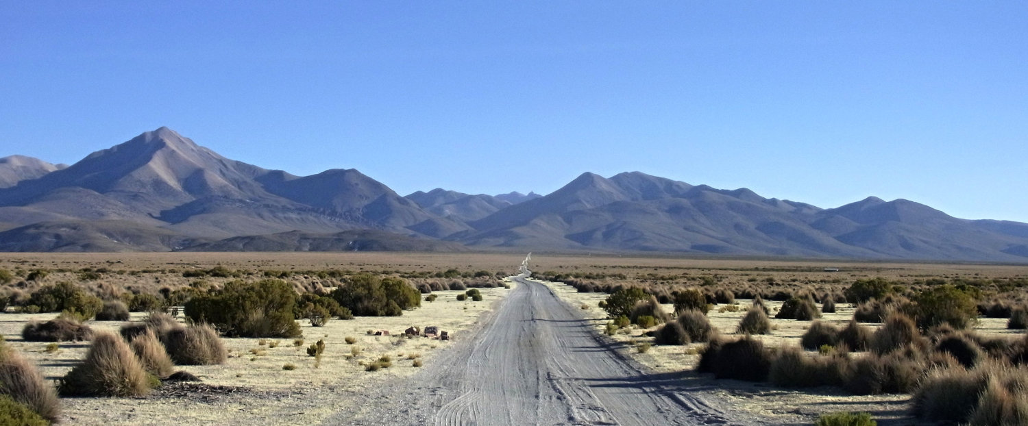 Bolivian alto plano - gravel road to vanishing point with mountains in the distance