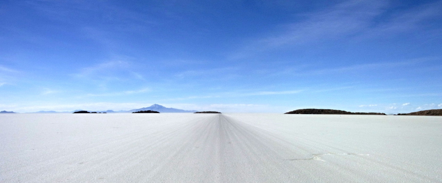 road going to vanishing point on the salar de uyuni with islands and mountains in the distance